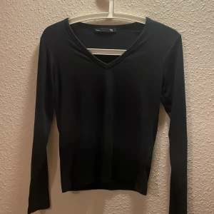 Svart v-ringad långärmad topp 157 - En stilren svart långärmad topp från 157 med v-ringning. Sitter snyggt och har en enkel, clean look som funkar till många olika outfits.