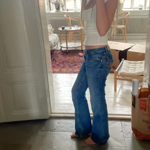 Blå bootcut jeans från Monki - Säljer ett par blå bootcut jeans från Monki med snygga broderade rosetter i orange på bakfickorna. Jeansen har låg midja och klassisk femficksdesign. Super söta🥰 nypris ca 500