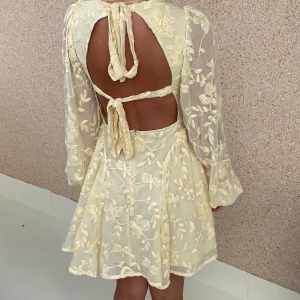 NA-KD gul klänning - Superfin ljusgul kortklänning med blommigt broderi och transparenta långärmar. Klänningen har v-ringning, volangig kjol och snygg öppen rygg med knytband. Köpt på NAKD för ca 2 månader sen, prislappen kvar🌸 Nypris 699:-