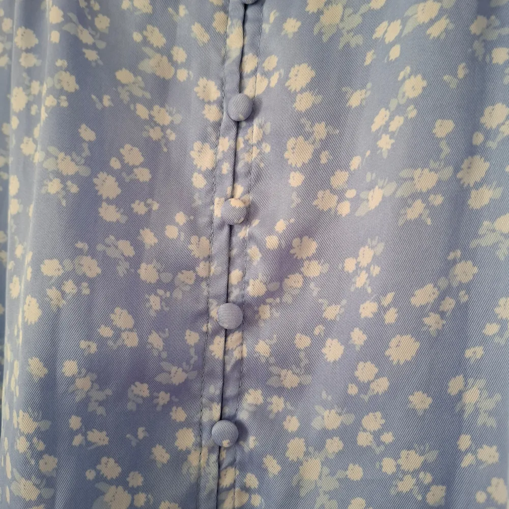 Charmig blå klänning med vita blommor från Neo Noir. Klänningen har trekvartsärmar och en v-ringad design med knappar framtill. Perfekt för vår och sommar!. Mekot.