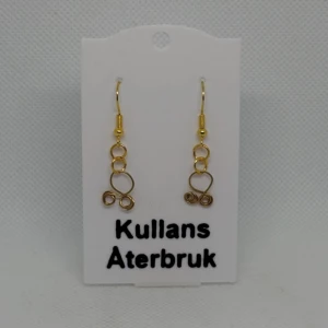 Trollkors örhängen från Kullans Återbruk - Snygga guldiga trollkors från Kullans Återbruk med en unik design av sammanlänkade cirklar och spiraler. Perfekta för att ge en elegant touch till din stil.
