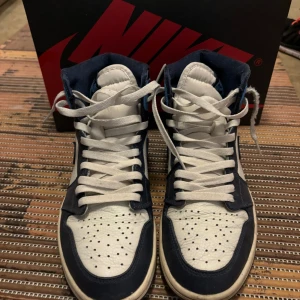 Jordan 1 obsidian - Snygga Nike Air Jordans i en fräsch kombination av blått och vitt. Skorna har en klassisk hög modell med snörning och den ikoniska Nike-loggan på sidan. Perfekta för dig som vill ha en stilren och sportig look.