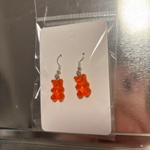 Orange örhängen med björndetalj - Snygga och lekfulla örhängen med orange björndetalj. Perfekta för att lägga till en färgglad touch till din outfit. Hängande design med silverfärgad krok. (Billigt material) 
