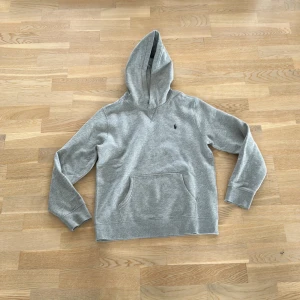 Grå hoodie från Polo Ralph Lauren - Säljer en stilren grå hoodie från Polo Ralph Lauren. Tröjan har en klassisk design med en känguruficka framtill och en liten broderad logga på bröstet. Perfekt för en avslappnad look. Använd ungefär 2 gånger och storlek XS-S i barn 🙌🏻 