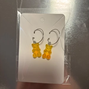 Örhängen med gummibjörnar - Snygga örhängen med orange gummibjörnar som hänger från silverfärgade ringar. Perfekta för att lägga till en lekfull touch till din stil. De är lätta och bekväma att bära hela dagen. (Billigt material) 