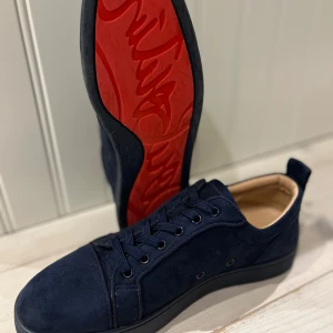  Feta mörk blåa Christian Louboutin  - Snygga mörkblå sneakers i mocka med en ikonisk röd sula. Skorna har snörning och en diskret broderad detalj på hälen. Perfekta för en stilren look. Köpta från Plick vet ej om dom är riktiga men tror det har knappt använt dem. Pris kan diskuteras vid snabb affär 