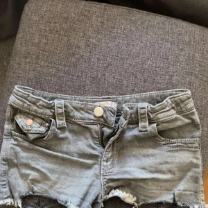 Lågmidjade jeansshorts f - Snygga grå lågmidjade jeansshorts från Gina Tricot med fransiga kanter och knappar på fickorna. Perfekta för en avslappnad stil. De har en klassisk design med bälteshällor och knappgylf.