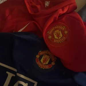 Manchester United fotbollströjor - Säljer två Manchester United fotbollströjor från Nike. En röd och en blå tröja, båda med klubbens emblem på bröstet. Perfekt för fans som vill visa sitt stöd för laget!