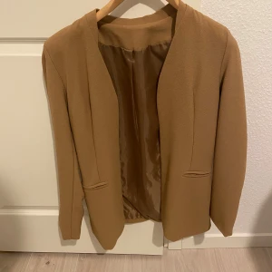 Beige kavaj - Snygg beige kavaj med en stilren design. Tillverkad i polyester med en mjuk insida. Perfekt för en elegant look. Tillverkad i Italien.