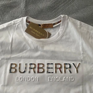 Vit t-shirt  - Snygg vit t-shirt från Brbery med deras ikoniska logga i relief på bröstet. Texten 'London England' är också tryckt under loggan. Perfekt för en stilren och klassisk look.