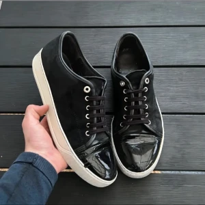Svarta sneaker från lanvin - Snygga svarta sneakers med glänsande lackdetaljer på tån och snörning. Skorna har en vit sula som ger en fräsch kontrast. Perfekta för en stilren look. Box tillkommer