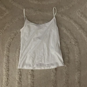 Vit linnetopp - Säljer en enkel och stilren vit linnetopp med smala axelband. Perfekt för lager-på-lager eller att bära som den är under varma dagar. Ett måste i garderoben för en minimalistisk look.