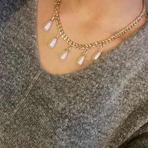 Maria Nilsdotter  - Elegant guldhalsband med droppformade pärlor som hänger längs kedjan. Perfekt för att ge en lyxig touch till din outfit. Kedjan är i en klassisk design som kompletterar de vita pärlorna. Liknar den från Maria Nilsdotter 