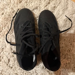 Svarta fotbollsskor med snörning - Snygga svarta fotbollsskor med snörning och mönstrad sula för bra grepp. Perfekta för fotbollsplanen och designade för att ge optimal prestanda.