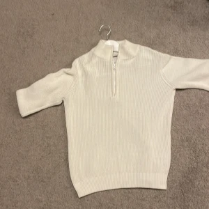 Vit ribbad tröja med dragkedja - Säljer en stilren vit ribbad tröja med dragkedja i halsen. Tröjan har en klassisk design med korta ärmar och en bekväm passform. Perfekt för en avslappnad look. Sise är L. Orginal pris 900