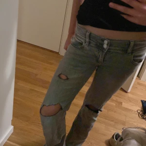 Grå jeans med slitningar - Snygga grå jeans med slitningar på knäna. De har en klassisk femficksdesign och en knappgylf. Perfekta för en avslappnad stil.