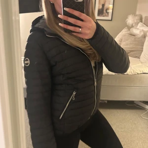 Svart dunjacka från Colmar - Säljer en snygg svart dunjacka från Colmar. Jackan har en figurnära passform med dragkedja framtill och två praktiska fickor med dragkedjor. Jackan är sparsamt använd o i fint skick utöver ett millimeter litet hål på armen (se bild ovan), dock inget som synds tydligt eller läggs märke till. Jackan sitter figurnära på mig som är 163cm lång och brukar vandligtvis ha storlek s/xs. Köpt på länna sport, nypris 3990kr. 