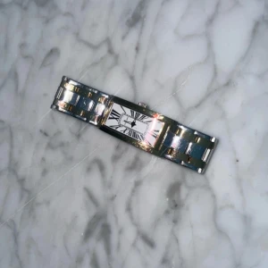 Elegant klocka med romerska siffror - Stilren klocka med rektangulär urtavla och romerska siffror. Armbandet är i metall med en mix av silver och guldtoner. Perfekt för en elegant look.