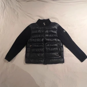 Mörkblå pufferjacka från Moncler - Säljer en snygg mörkblå pufferjacka från Moncler med dragkedja och ribbad krage. Storlek ( 6 ) Jackan har långa ärmar och ett stilrent märke på ärmen. Perfekt för kyligare dagar med sin quiltade design och klassiska look.