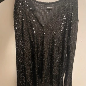 Svart glittrig tröja från Gina Tricot - Snygg svart tröja från Gina Tricot med glittriga paljetter över hela ytan. Tröjan har en v-ringad design och långa ärmar, perfekt för en festlig kväll.