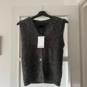 Grå stickad väst från Monki - Säljer en  grå stickad väst från Monki med v-ringning och knappdetalj framtill. Helt oanvänd! 