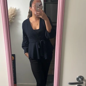 Marinblå omlottopp med knyt - Snygg marinblå omlottopp med knyt i midjan. Toppen har långa ärmar och en v-ringad design som ger en elegant look. Perfekt för att klä upp eller ner beroende på tillfälle.