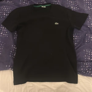 Svart Lacoste t shirt - Snygg svart t-shirt från Lacoste med det klassiska krokodilemblem på bröstet. Perfekt för en stilren och avslappnad look. Kortärmad och i mjukt material för extra komfort.
