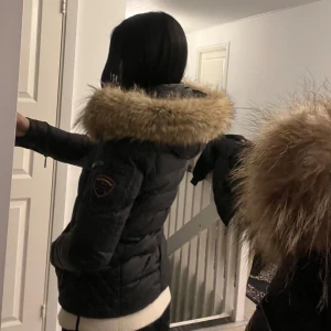 Svart dunjacka med päls - Säljer en snygg svart RockAndBlue dunjacka med en stor huva kantad av päls. Jackan är i jättebra skick, använd i en vinter. Pälsen är äkta. Mera bilder skickas priv