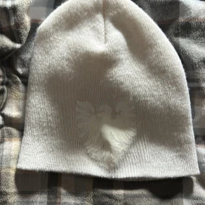 Tuttolente mössa - Snygg vit mössa med ett diskret tryck av en örn på framsidan. Perfekt för att hålla värmen under kyliga dagar. Enkel och stilren design som passar till det mesta.