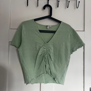 Grön kortärmad topp från Aware - Säljer en ljusgrön topp från Aware med korta ärmar och en snygg v-ringning. Toppen har en ribbad struktur och en knytning framtill som ger en fin detalj. Perfekt för en avslappnad stil.