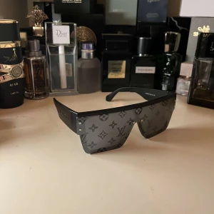 Svarta solglasögon från Louis V - Snygga svarta solglasögon från Louis  V med ett monogrammönster på glasen. De har en modern, kantig design och breda skalmar. Perfekta för att ge en lyxig touch till din stil. Priset kan diskuteras. Frågor,skriv!