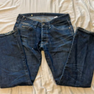 Blå jeans från G-Star RAW - Säljer ett par snygga blå jeans från G-Star RAW. De har en klassisk femficksdesign med coola detaljer på bakfickorna. Perfekta för en avslappnad stil. Passar bra till sneakers eller kängor.