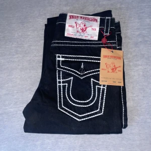 Svarta jeans från True Religion - Snygga svarta jeans från True Religion med kontrasterande vit söm. Klassisk femficksdesign och tydlig logga på bakfickorna. Perfekta för en stilren look. helt nya har aldrig använt 