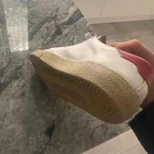 Vita sneakers från Saint Laurent - Snygga vita sneakers från Saint Laurent med en stilren design. Skorna har en röd detalj på hälen och klassisk snörning framtill. Perfekta för en trendig look allt är og och i man ser nötningar på sidorna