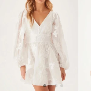 Vit blommig klänning perfekt till studenten! - Säljer en vacker vit klänning med blommigt mönster och spetsdetaljer. Klänningen har en v-ringad design och långa ärmar. Perfekt för sommarens festligheter! Aldrig använd💕