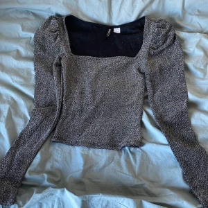 Glittrig topp från HM - Säljer en glittrig topp från HM med fyrkantig halsringning och långa ärmar. Perfekt för en kväll ute eller festliga tillfällen. Toppen har en figurnära passform och är i en snygg silverfärg.
