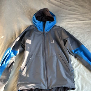 Haglöfs jacka - Säljer en grå och blå vindjacka från Haglöfs. Jackan har en justerbar huva och dragkedja framtill. Perfekt för utomhusaktiviteter med sin funktionella design och slitstarka material.