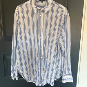 Skjorta från Massimo Dutti - Säljer en stilren blå och vit randig skjorta från Massimo Dutti. Skjortan har långa ärmar och knappar framtill. Ej använd bara tvättad en gång. Storlek M