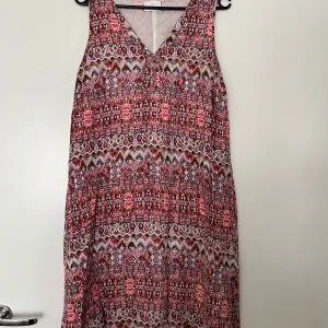 Klänning, KAFFE, multifärgad, 36 - Ärmlös klänning med V-ringning och ett färgstarkt, abstrakt mönster i rosa, vitt och andra nyanser. Från Kaffe i storlek 36. Klänningen har ett tunt foder under. Klänningen är i nyskick. 100% viskos.   Mått: Längd ca 90 cm Byst ca 40 cm Midja ca 45 cm