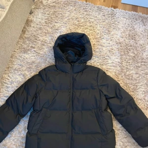 Svart pufferjacka från ONLY - Säljer en svart pufferjacka från ONLY. Jackan har en huva och är perfekt för kyliga dagar. Den har en stilren design med dragkedja framtill och långa ärmar. Perfekt för att hålla värmen under vintern.