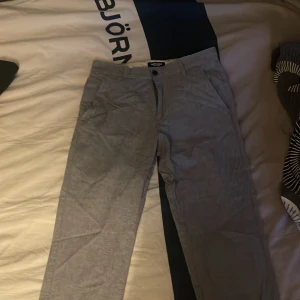 Grå chinos från Jack & Jones - Snygga grå chinos från Jack & Jones med en klassisk design. Byxorna har en normal passform och är tillverkade i ett bekvämt material. Perfekta för en stilren look.