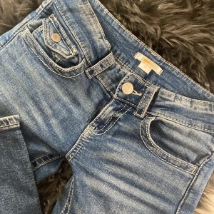 Blå jeans med broderade fickor - Snygga blå low rise jeans med unika broderade detaljer på bakfickorna. De har en klassisk femficksdesign och en knappgylf. Perfekta för en avslappnad stil med en touch av personlighet. Skriv för flera bilder 💘😽