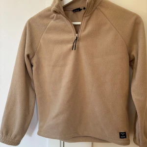Beige fleece tröja med dragkedja från Lager 157 - Säljer en mysig beige fleece tröja med halv dragkedja och hög krage. Perfekt för kyliga dagar. Tröjan har långa ärmar och en enkel design som passar till det mesta. .