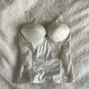 Vit korsett med spetsdetaljer - Elegant vit korsett med vackra spetsdetaljer och justerbara axelband. Den har en blommig design och hakknäppning bak. Perfekt för en stilfull look. Skriv vid frågor💞