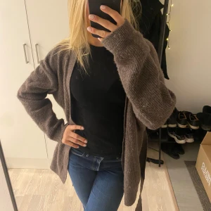 Brun stickad kofta med bälte - Mysig brun stickad kofta med långa ärmar och ett matchande bälte i midjan. Perfekt för kyliga dagar och ger en avslappnad stil. Koftan har en öppen design och är lätt att matcha med olika outfits.