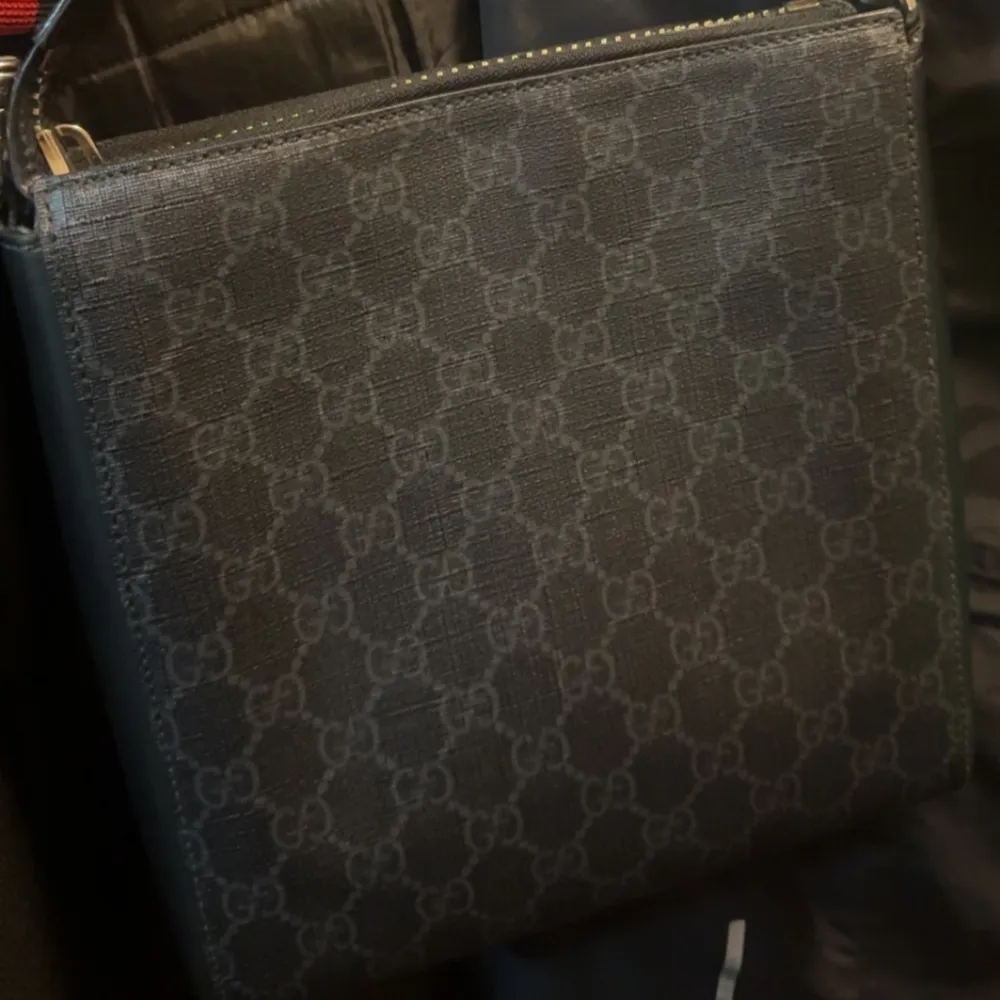 Snygg svart axelväska från Gucci med det klassiska monogrammönstret. Väskan har en justerbar axelrem i rött och blått samt en praktisk dragkedja på framsidan. Perfekt för att bära dina nödvändigheter med stil. Ny. Laukut & Käsilaukut.