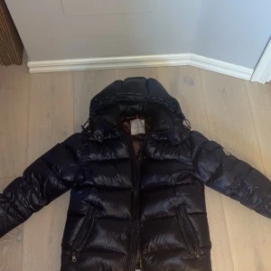 Svart pufferjacka från Moncler - Säljer en snygg svart pufferjacka från Moncler. Jackan har en quiltad design med dragkedja och en praktisk huva. Perfekt för kyliga dagar.