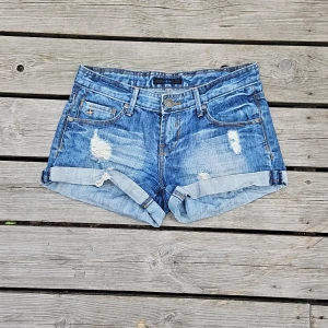 Låga jeansshorts  - Lågmidjade blå jeansshorts med blekning och slitningar, extremt fina. Normala i storlek - 38cm tvärs över, 79 runt om hela! Storlek XS, från AC perfekta till i sommar 💕