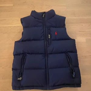 Ralph lauren väst - Mörkblå Ralph Lauren väst.  Mycket sparsamt använd, ser ut som ny. Storlek M junior motsvarar ungefär strl 150/160. Hanken att hänga upp jackan har dock gått av men kan såklart lätt fixas för den som köper. 