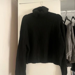 Svart stickad polotröja från H&M - Svart, ribbstickad polotröja från H&M i storlek S. Tröjan har en hög polokrage och är långärmad med en lite loose passform. Perfekt för kyliga dagar och enkel att matcha med jeans eller kjol.